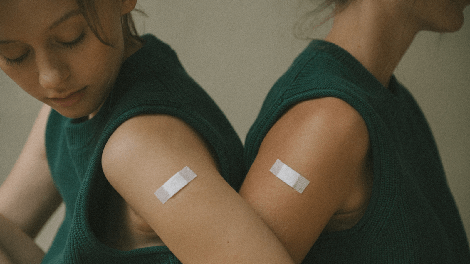 two women sitting back to back with plasters on their upper arms